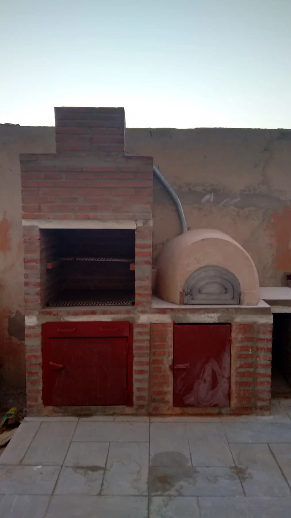 Barbecue en briques avec four à dôme intégré et portes métalliques rouges