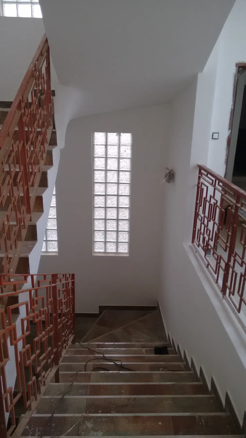 Escalier vu d'en haut : garde-corps métalliques géométriques, fenêtre en briques de verre