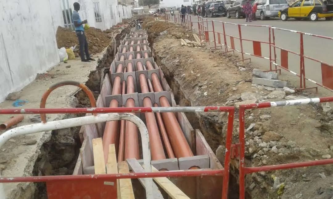 Tranchée de câbles électriques : fourreaux alignés sur cales béton entre barrières de sécurité