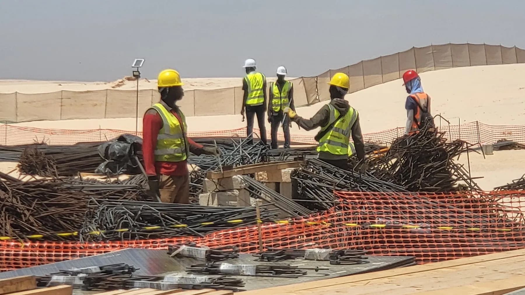 Équipe chantier en casques et gilets haute visibilité au travail sur un tas d'armatures