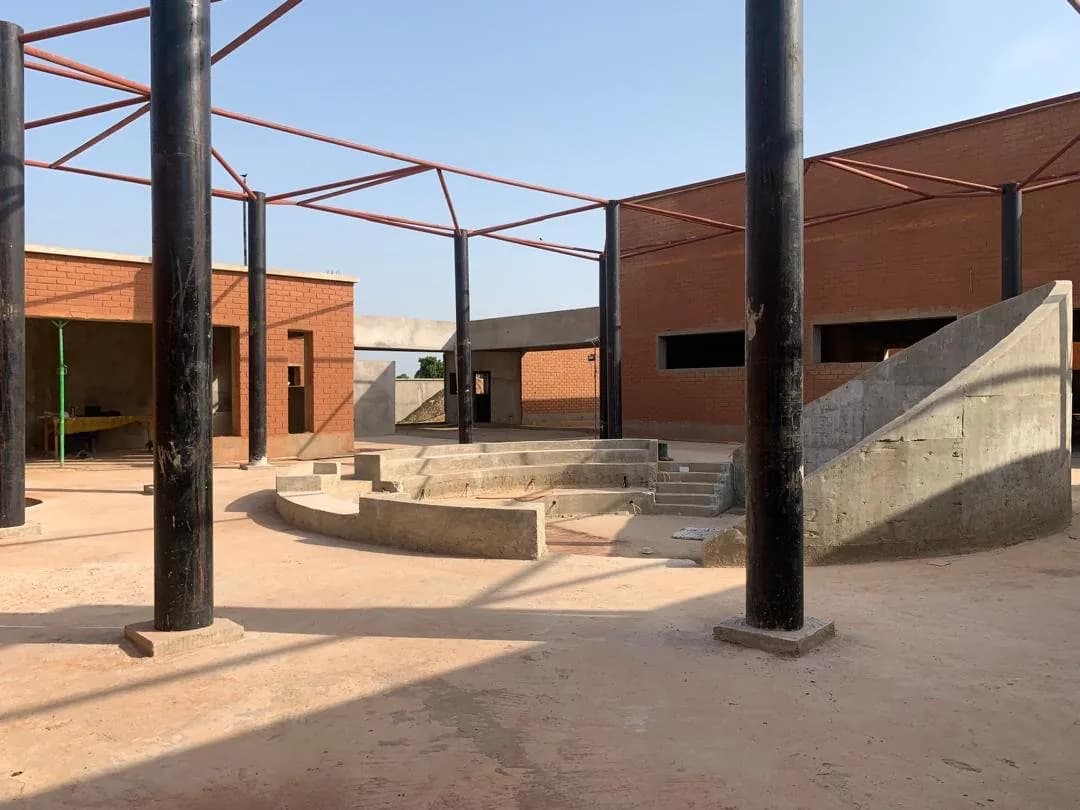 Chantier d'un équipement public : amphithéâtre en gradins, murs en briques rouges et charpente métallique