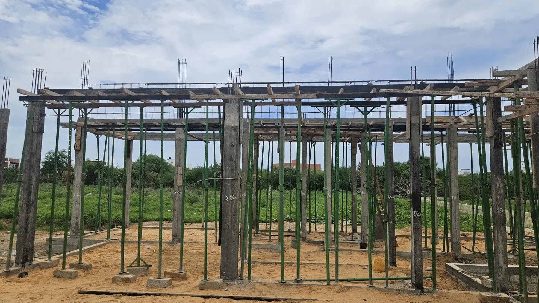 Ossature en béton armé avec poteaux et étaiements verts sous un ciel nuageux
